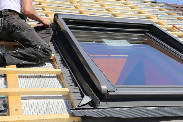 Artisan couvreur en plein travail de pose et réglage de fenêtre de toit Velux sur liteaux